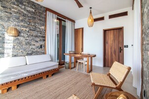 Una habitación moderna con pared de piedra, cama de madera, mesa de comedor con sillas y ventilador de techo.