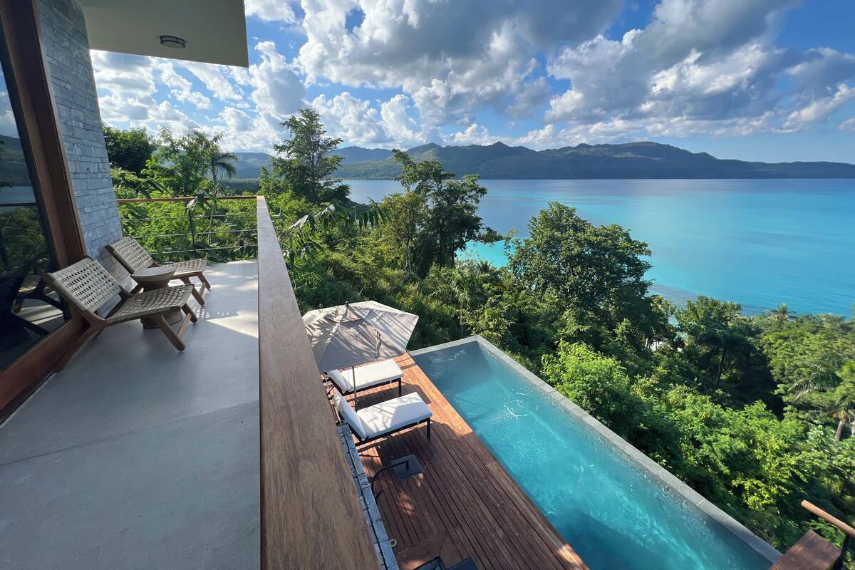 A poolside area with lounge chairs and a view of a large body of water and mountains.