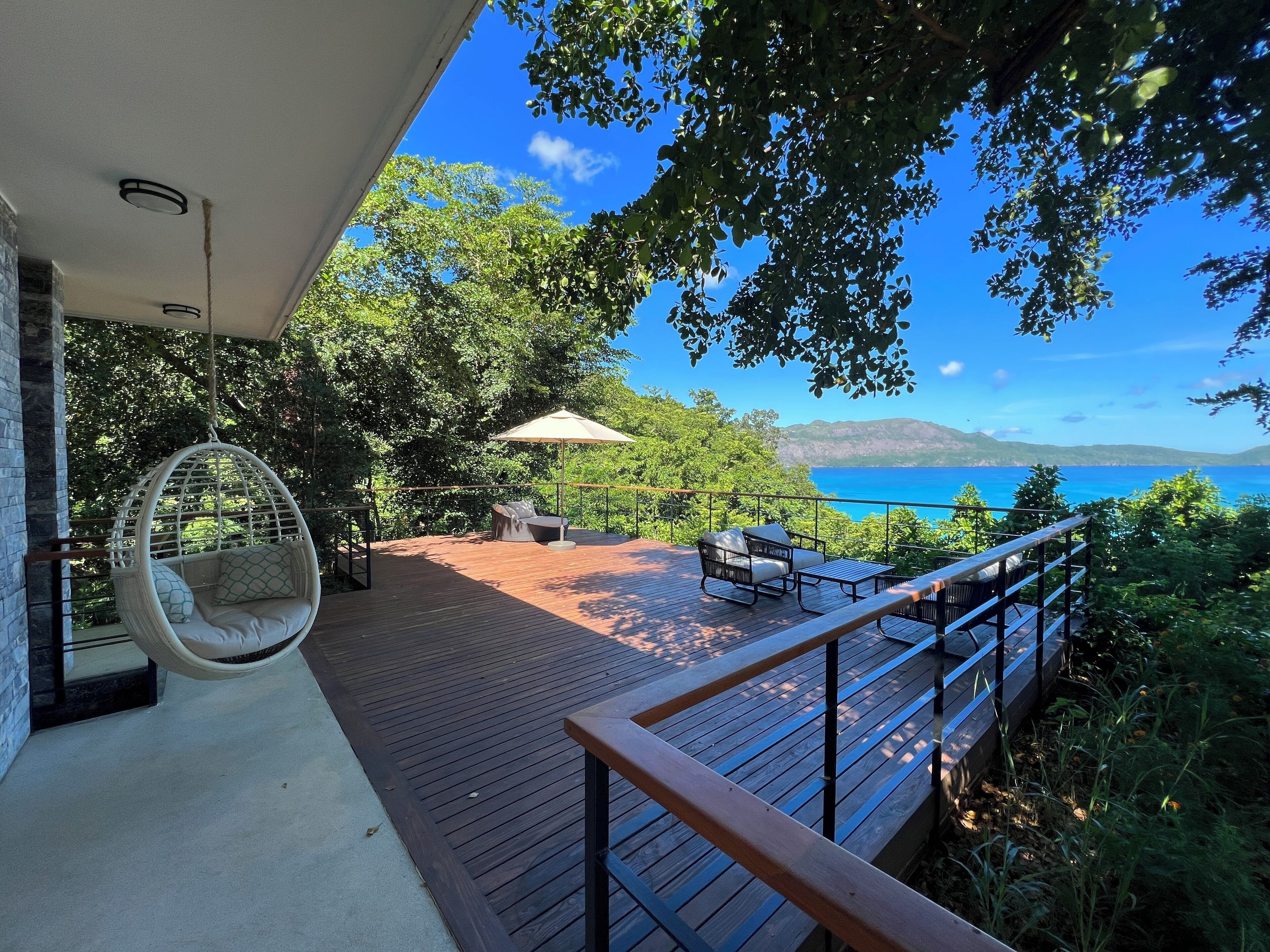 Une terrasse en bois avec des sièges d’extérieur, un fauteuil suspendu et une vue sur la mer.