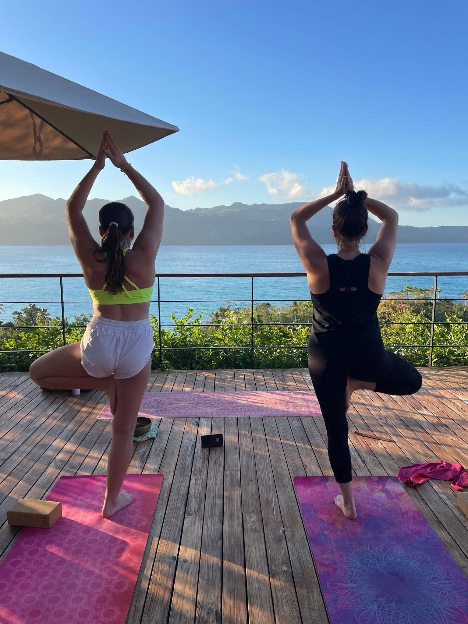 Two individuals practicing yoga on a wooden deck with a scenic ocean view.