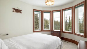 Une chambre avec un grand lit, une commode et une fenêtre donnant sur la forêt.