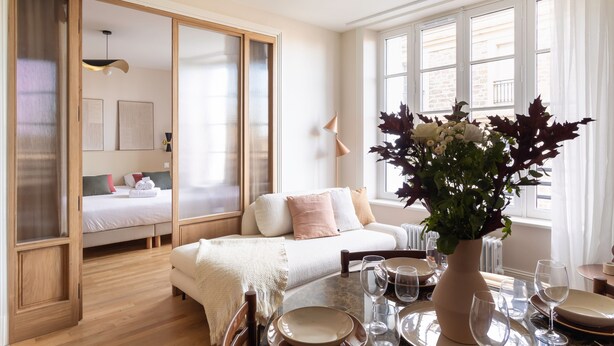 Ein modernes Hotelzimmer mit einem großen Bett, einem Esstisch für zwei Personen und Blick auf die Stadt durch große Fenster.