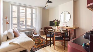 Ein gemütliches Wohnzimmer mit einer Couch, einem Couchtisch und einem Essbereich mit Stühlen und Tisch. Ein Kamin, ein großes Fenster und ein an der Wand befestigtes Fernsehgerät sind vorhanden.