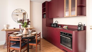Eine moderne Küche mit roten Schränken, einem eingebauten Backofen und einem Essbereich mit einem Holztisch und Stühlen.