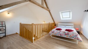 A bedroom with a sloped ceiling, a wooden staircase, a bed with floral bedding, and a skylight. - La Maison du Puits Merpault - Avec jardin (Saint-Alban)