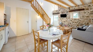 A spacious living area with a stone wall, wooden ceiling beams, a dining table with chairs, and a sofa. - La Maison du Puits Merpault - Avec jardin (Saint-Alban)