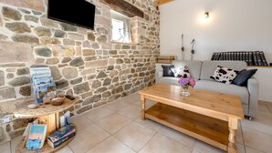 A cozy living room with a stone wall, a mounted TV, a wooden coffee table, and a sofa with cushions. - La Maison du Puits Merpault - Avec jardin (Saint-Alban)