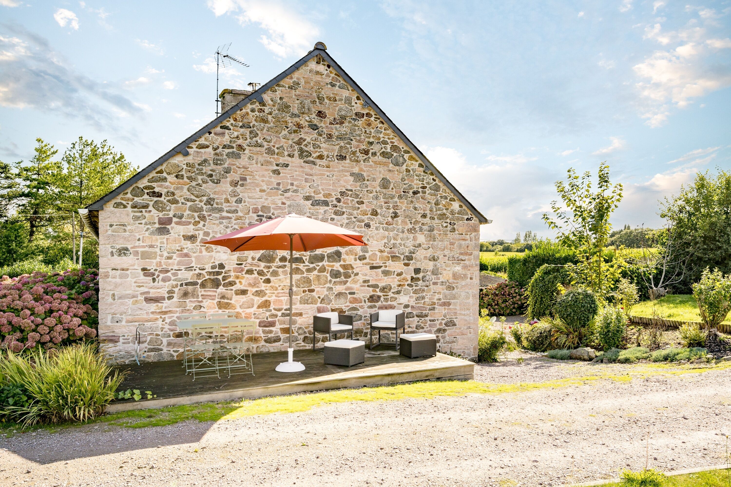 A stone building with a patio area featuring outdoor furniture and a red umbrella.