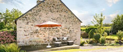 A stone building with a patio area featuring outdoor furniture and a red umbrella.