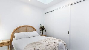 Un dormitorio con cama, mesita de noche, repisa y estante montado en la pared, además de una puerta corredera.