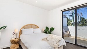 Un dormitorio moderno con una cama grande, una mesita de noche con lámpara y vistas al balcón exterior.