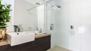 Un baño moderno con cabina de ducha de vidrio, un lavabo blanco y un mueble de tocador de madera oscura.