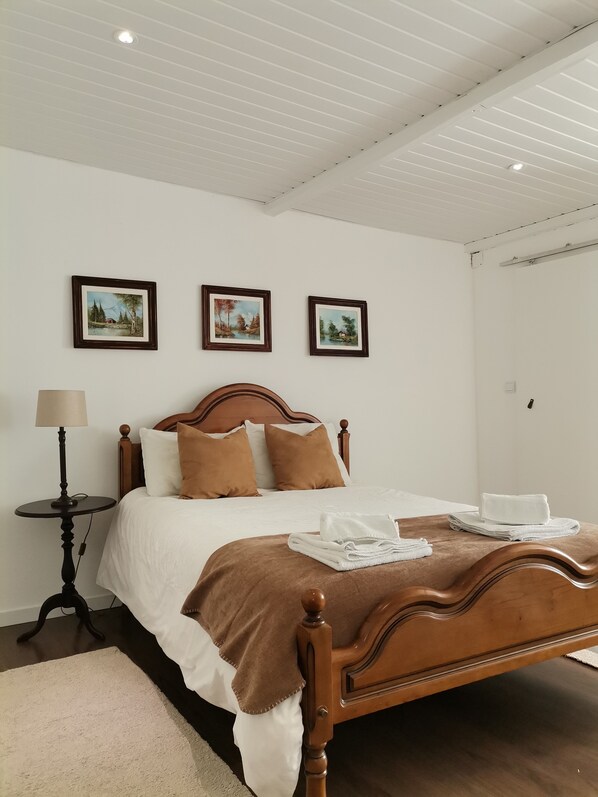 A neatly made bed with a wooden headboard, white bedding, and brown pillows. There are three framed pictures on the wall above the bed. - Casa Cadu - Porto (Porto)