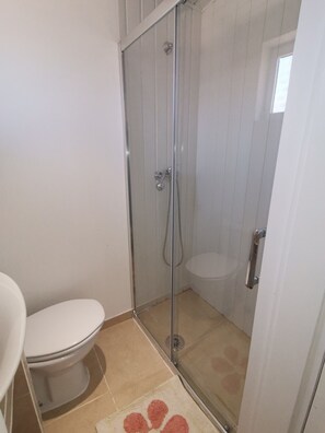 A bathroom with a toilet, a glass-enclosed shower, and a beige floor. - Casa Cadu - Porto (Porto)
