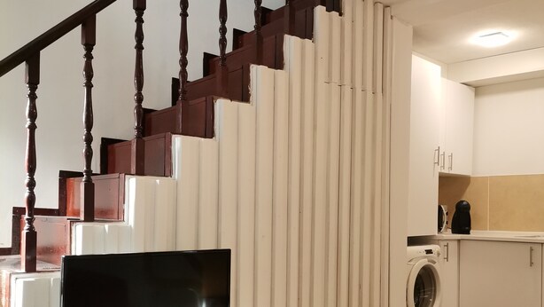 A modern living room with a flat-screen TV, a washing machine, and a staircase with wooden balusters. - Casa Cadu - Porto (Porto)