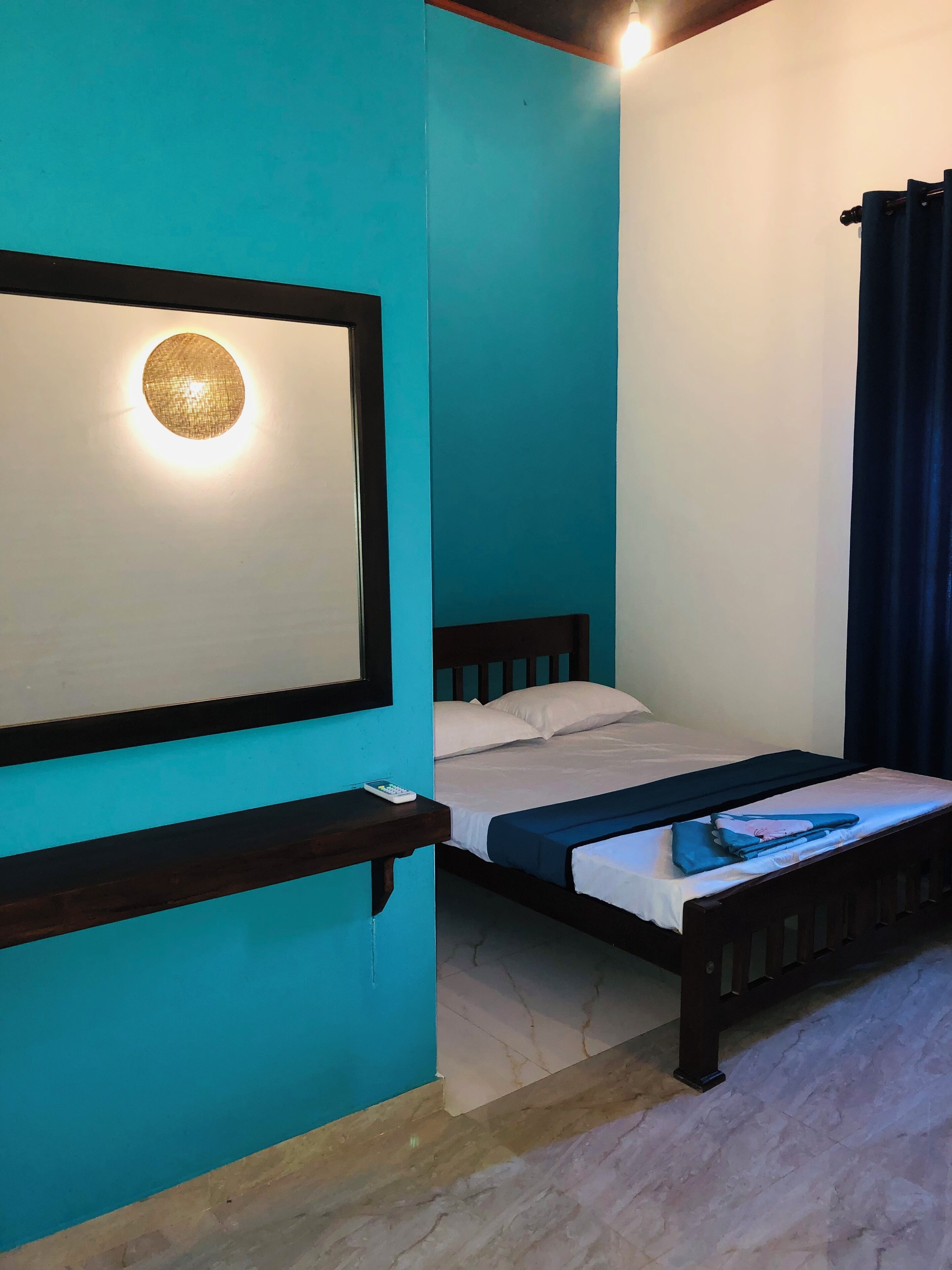 Une pièce aux murs de couleur turquoise, un lit avec une tête de lit en bois, une table de chevet avec une télécommande et un luminaire fixé au mur.