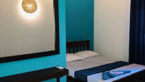 Una habitación con paredes color turquesa, una cama con cabecera de madera, una mesita de noche con un control remoto y una lámpara de pared.