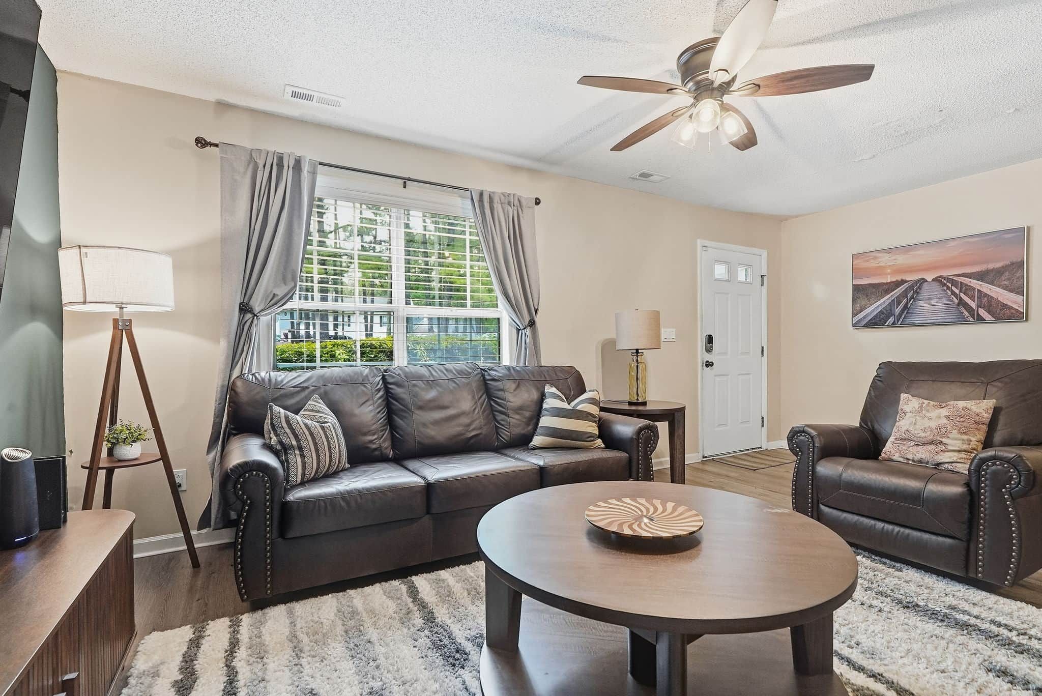 A living room with a leather sofa, a round coffee table, a floor lamp, and a ceiling fan.
