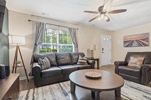 A living room with a leather sofa, a round coffee table, a floor lamp, and a ceiling fan.