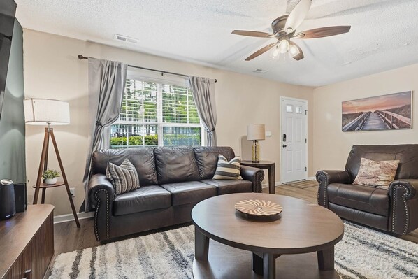 A living room with a leather sofa, a round coffee table, a floor lamp, and a ceiling fan.