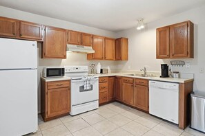 A kitchen with wooden cabinets, a white refrigerator, a microwave, an oven, a sink, and a dishwasher.