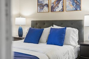 Une chambre d’hôtel avec un lit, deux tables de chevet, une lampe et trois tableaux abstraits accrochés au mur.