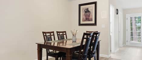 Un comedor con una mesa y sillas de madera, un jarrón con flores secas y un cuadro en la pared.
