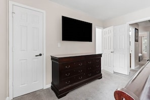 A hallway with white doors, a dark wooden dresser, and a mounted television on the wall.