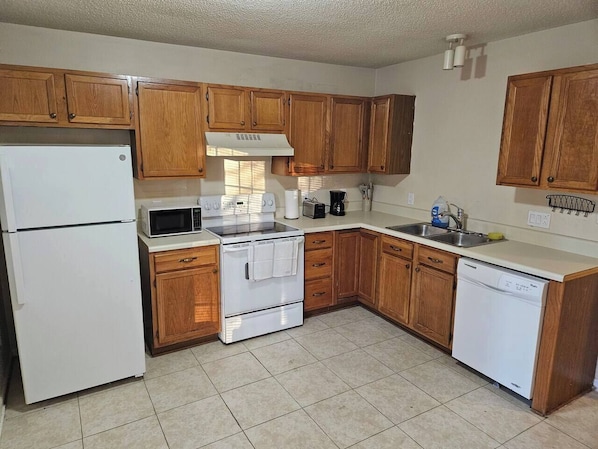 A kitchen with wooden cabinets, a white refrigerator, a microwave, a stove, a dishwasher, and a sink.