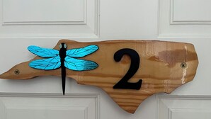 Un panneau en bois indiquant le numéro de la maison, orné d’un motif de libellule.