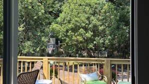 Une terrasse en bois, aménagée avec du mobilier d’extérieur comprenant des chaises et une table, donnant sur un jardin avec des arbres et un panier de basketball.