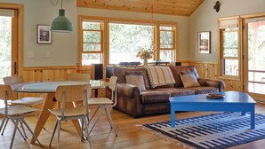 Una sala de estar amplia con techo de madera, un sofá de cuero marrón, una mesa de centro azul y un comedor con una mesa redonda y sillas.