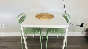 A white table with a woven placemat, surrounded by four green chairs. - Quiet studio in New Port Richey Downtown. Apartment B (New Port Richey)