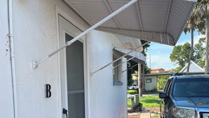 A covered outdoor area with a car parked nearby, a door labeled 'B', and a pathway leading to a house. - Quiet studio in New Port Richey Downtown. Apartment B (New Port Richey)