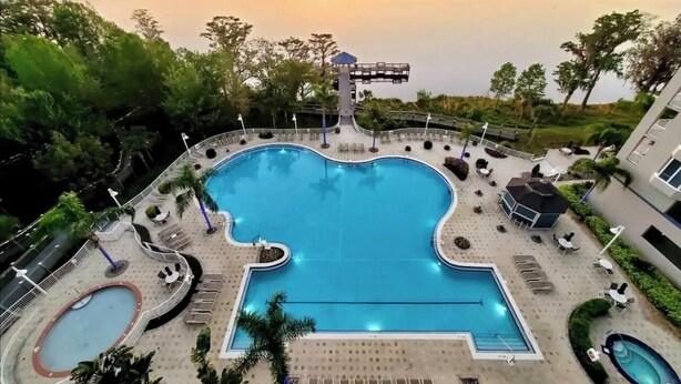 Une piscine à la forme originale, entourée de chaises longues et d’une petite terrasse, d’où l’on peut admirer un plan d’eau au coucher du soleil.