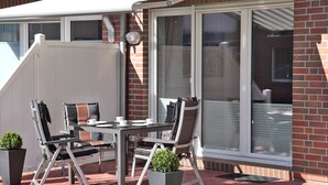 Patio esterno con tavolo e sedie, zona relax coperta e parete in mattoni con una porta scorrevole in vetro.