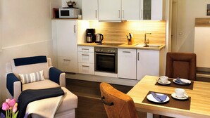 Una cucina compatta con mobili bianchi, un forno a microonde, una macchina da caffè e un lavello. C'è un tavolo da pranzo con sedie e un vaso di fiori.