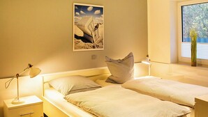 Una camera da letto con due letti, un comodino con una lampada, una finestra con tende e un quadro appeso al muro.