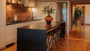 A modern kitchen with a central island, bar stools, and a brick backsplash.