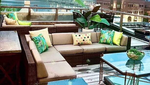 A rooftop terrace with a sofa set, a glass table, and string lights.