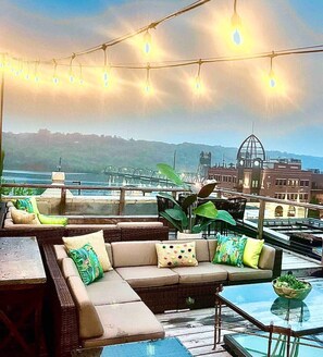 A rooftop terrace with a sofa set, a glass table, and string lights.