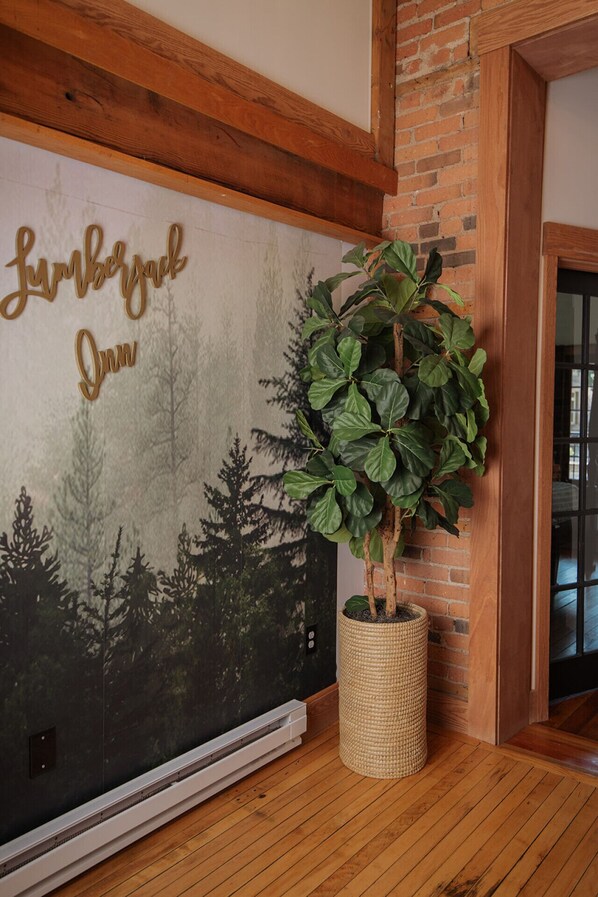 A room with a large wall mural depicting a forest scene, a potted plant, and a wooden ceiling beam.