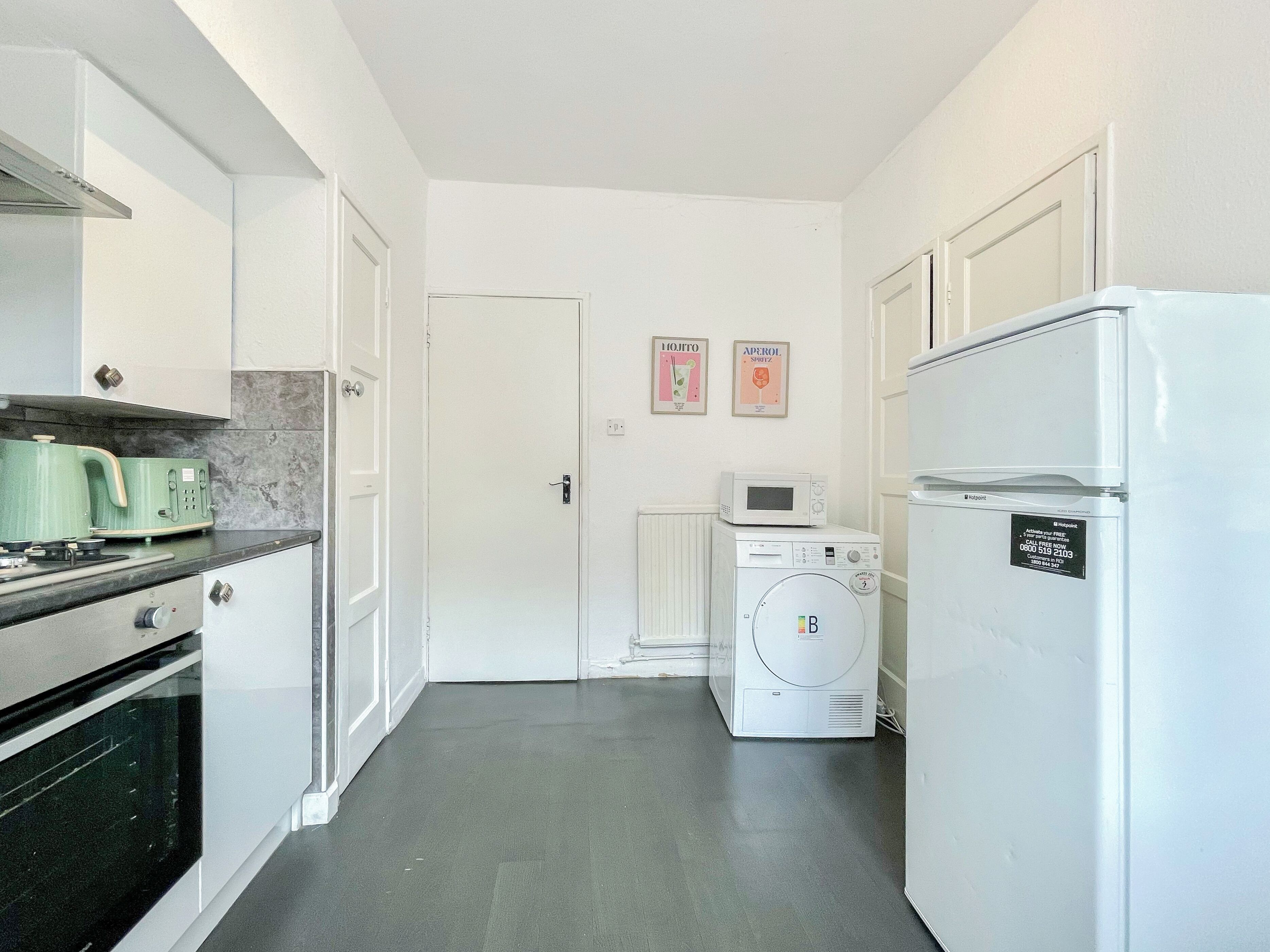 A compact kitchen with white cabinets, a stove, a microwave, and a refrigerator. There is a washing machine in the corner.