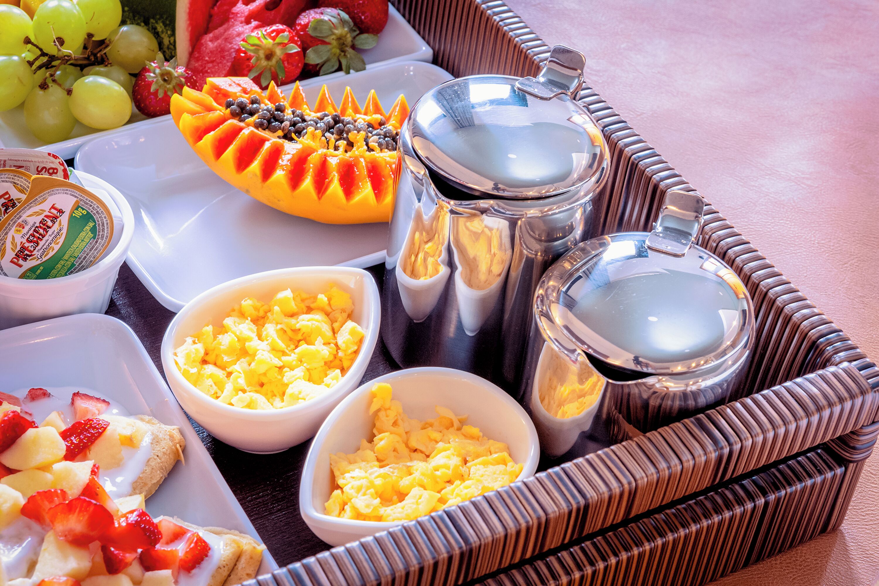 A breakfast tray with scrambled eggs, fruit, yogurt, and coffee.