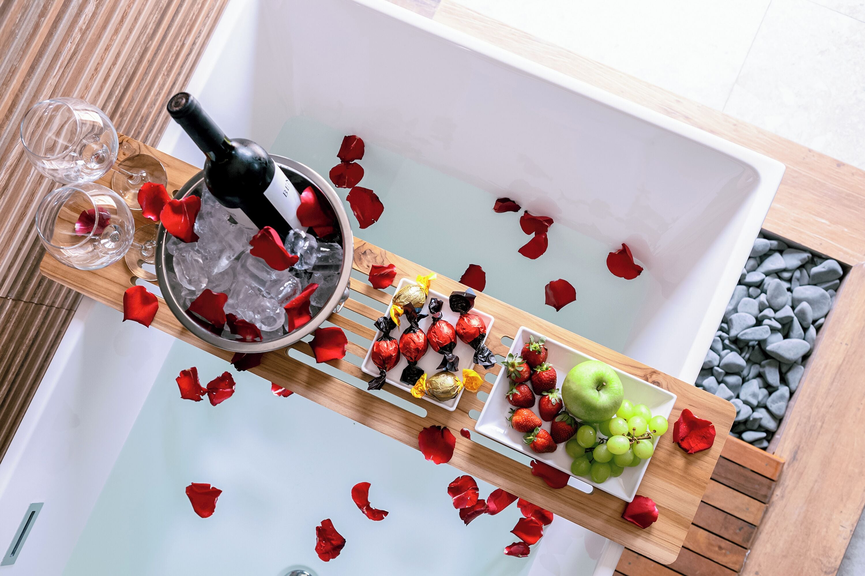 Un plateau avec une bouteille de vin, des verres vides, des fraises, des raisins et des pétales de rose.