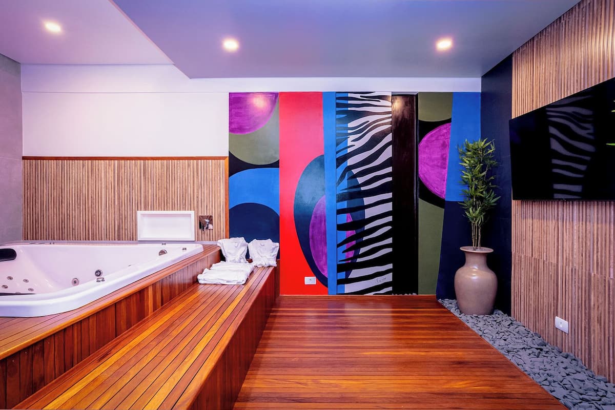 Um banheiro moderno com piso de madeira, uma banheira grande e arte abstrata colorida nas paredes.