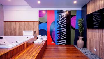 Un baño moderno con piso de madera, una bañera grande y arte abstracto colorido en las paredes.