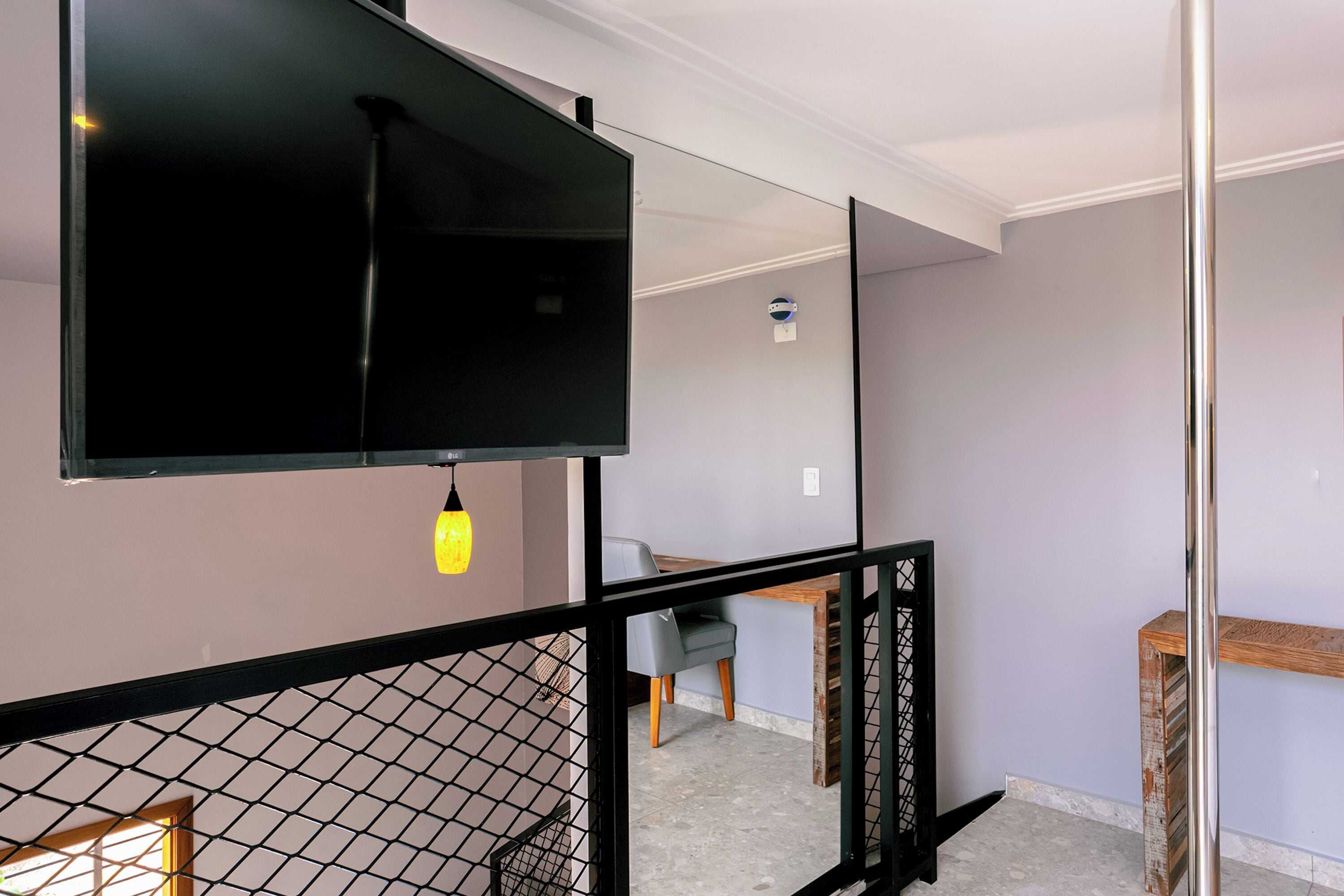 A modern interior with a flat-screen TV mounted on a wall, a dining area with a table and chairs, and a staircase with a metal railing.