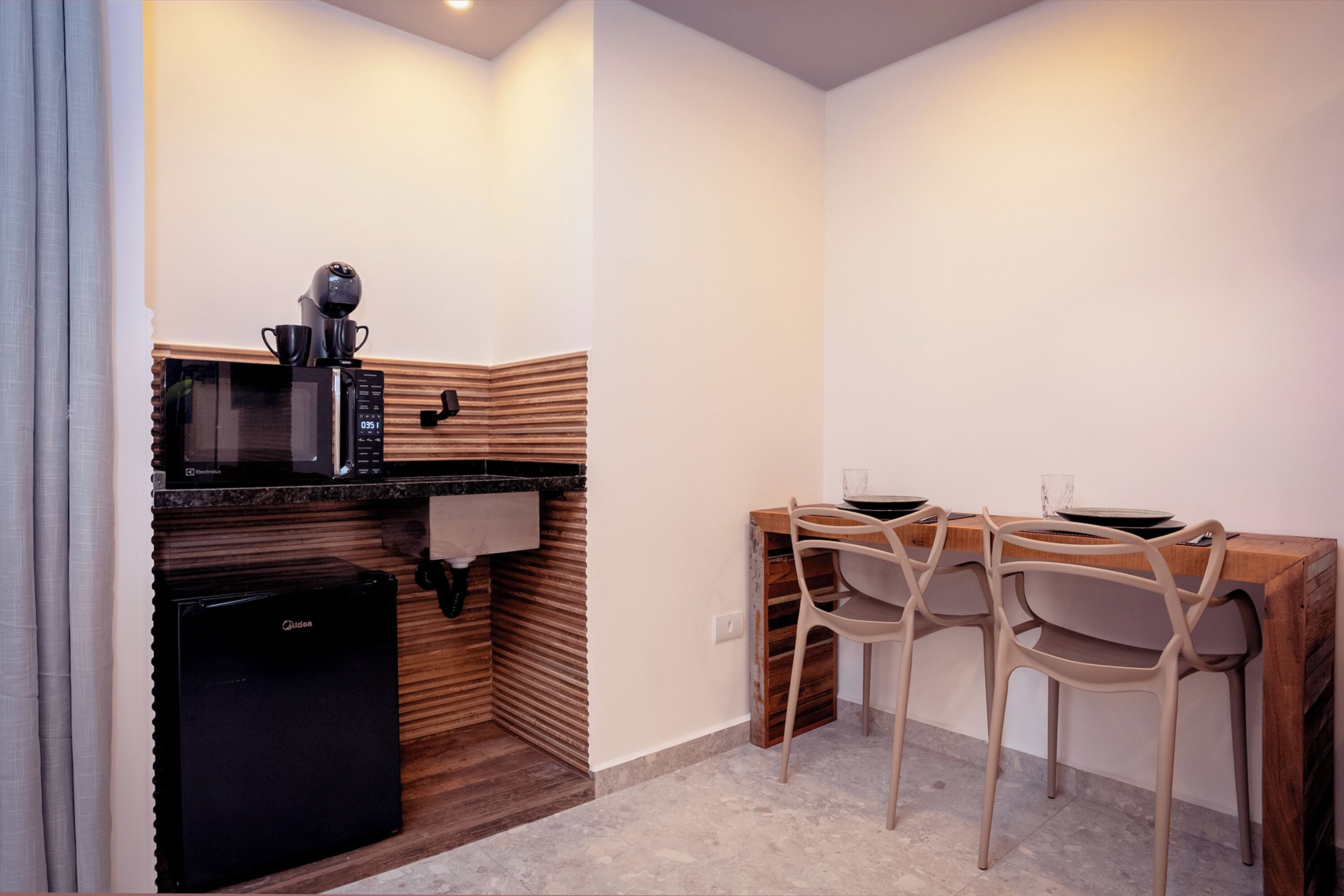 A compact kitchen with a microwave, coffee maker, and a small refrigerator. There is a wooden bench with chairs and a small table.