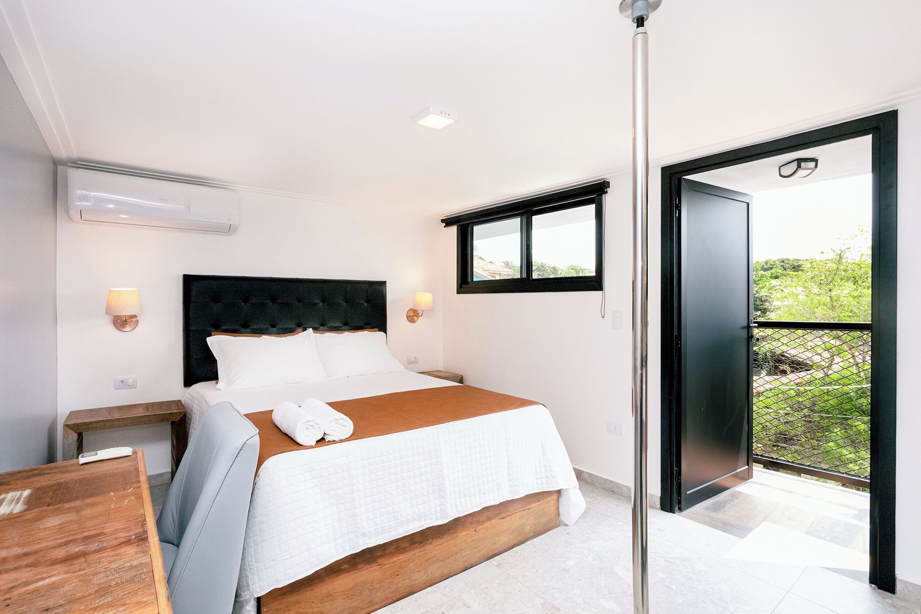 Un dormitorio moderno con una cama grande, cabecera de madera, lámparas de noche, una ventana y una puerta al balcón.